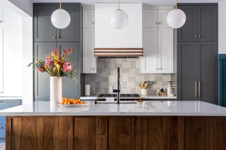 Modern kitchen with a marble island, wood cabinets, and globe pendant lights—perfect for showcasing a luxury multifamily real estate sale in California. Features include geometric tile backsplash and premium appliances.